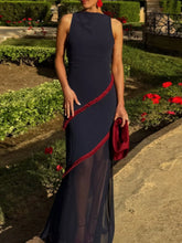 Woman in a navy dress with red trim standing in a garden.